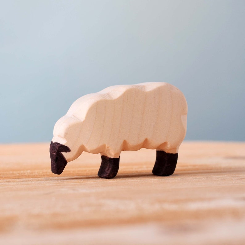 A single wooden sheep toy from a profile view, illustrating the contrast between its light body and dark face and legs.