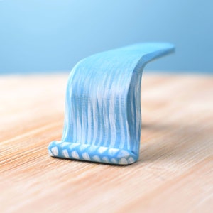 Single wooden waterfall piece with streaks of white and blue, simulating water cascading down, set upright on a wooden table.