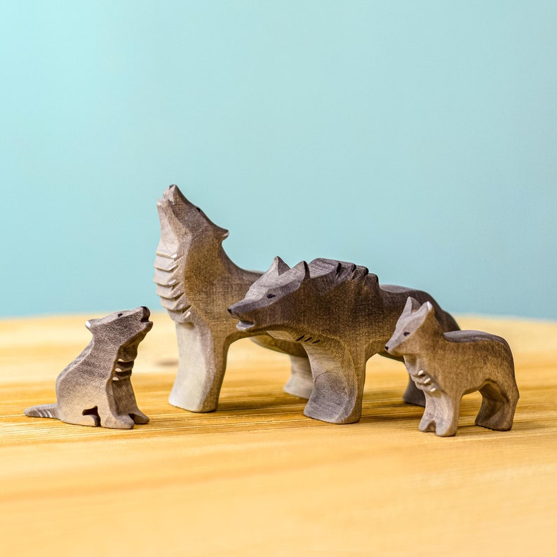 Handcrafted wooden wolf pack figures with one large wolf howling, another standing, and a small wolf cub, all on a wooden surface against a blue background.