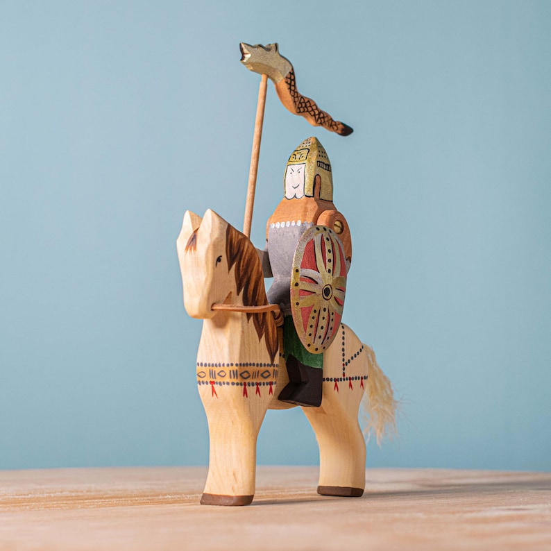 Artisanal wooden knight mounted on a horse, holding a lance with a fox-shaped flag, capturing the essence of medieval toy craftsmanship against a blue background.