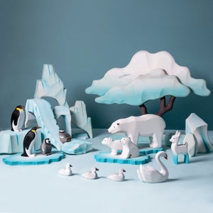 Wooden animal figures including penguins, polar bears, and swans among wooden icebergs set against a teal background.