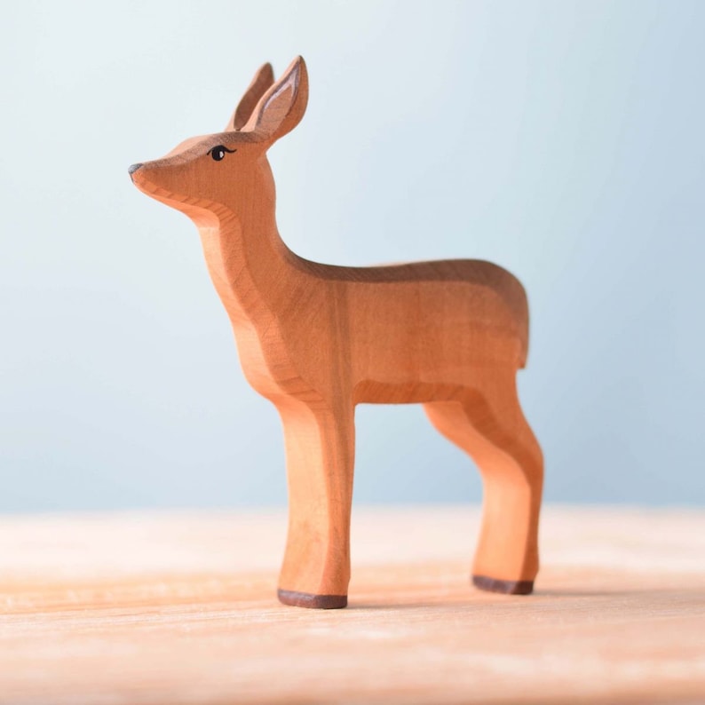 A wooden figurine of a deer standing on a smooth surface, with a soft blue background that provides a tranquil setting, is a unique handmade gift.