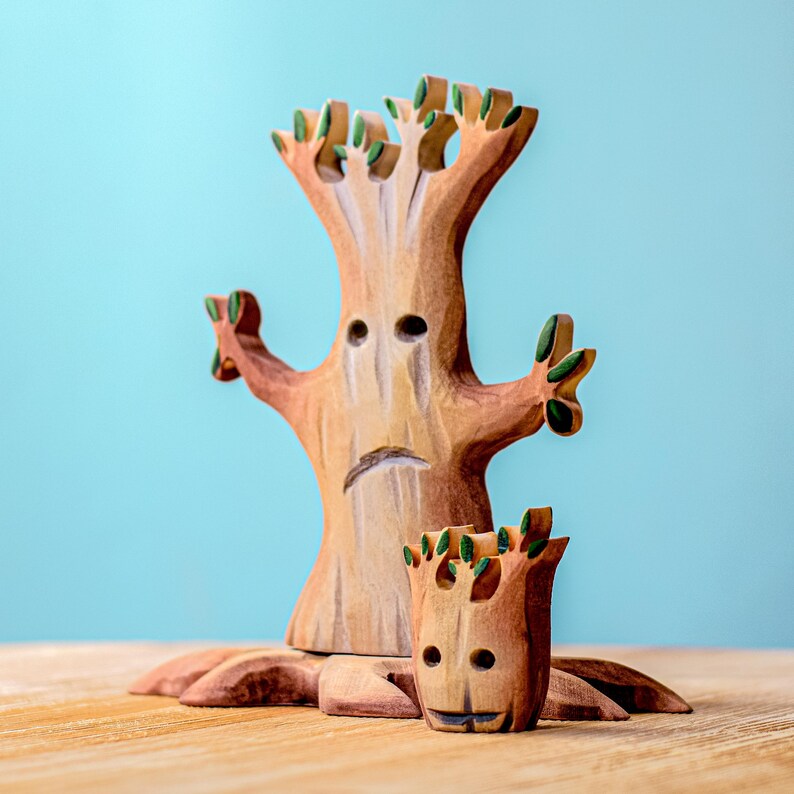 Large wooden spooky tree with a saddened face surrounded by green leafy branches and a smaller tree stump, all set against a turquoise backdrop.