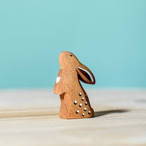 Handcrafted wooden bunny toy with heart and polka-dot cut-out details, displayed against a soft teal background.