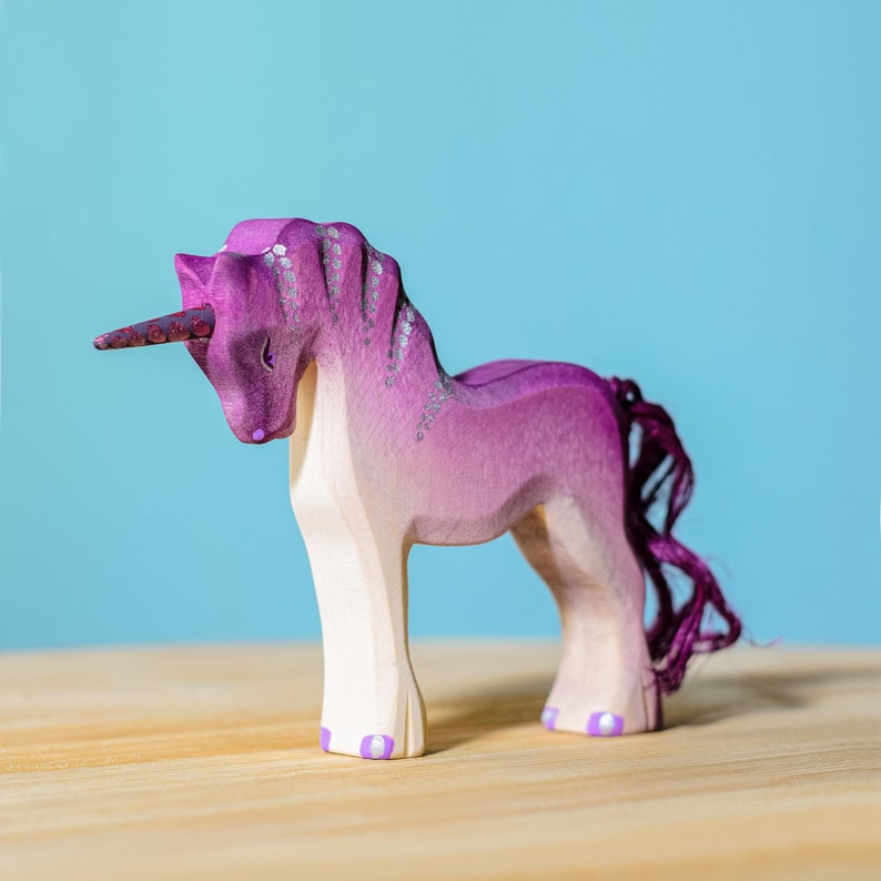 Pink unicorn toy made of wood, displayed on a wooden table.