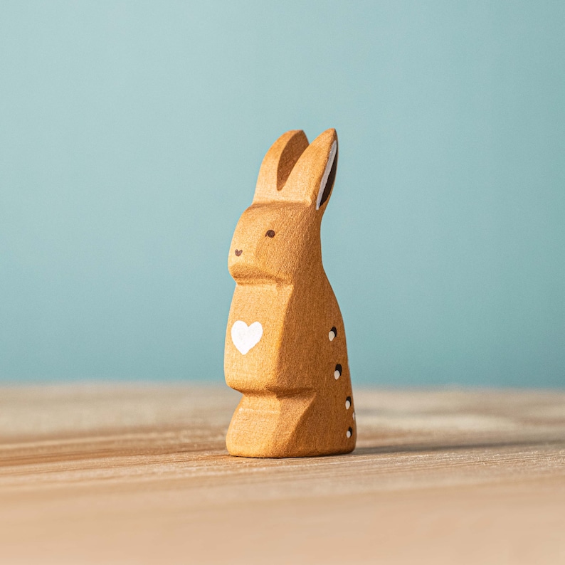 A charming wooden rabbit figurine with a white heart on its chest, set against a serene blue background, making it a unique handmade gift.