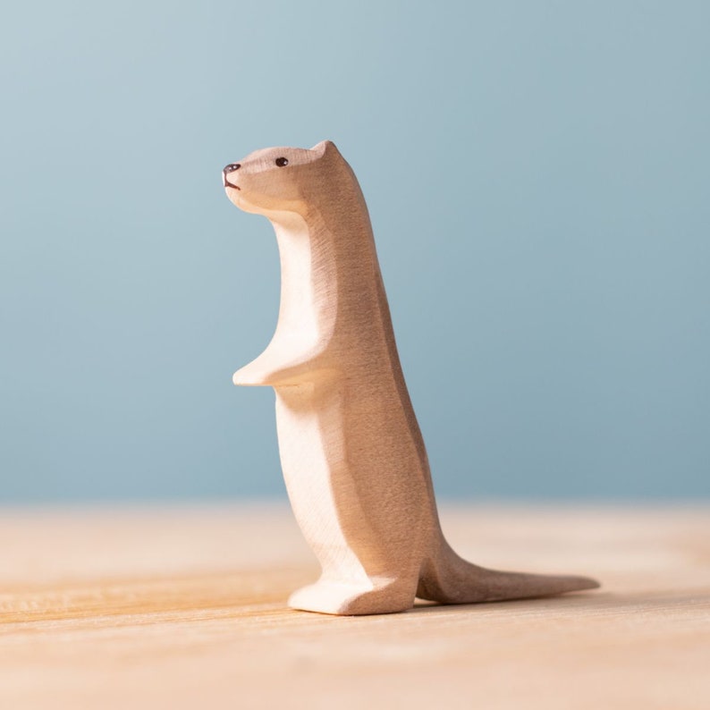 Upright wooden otter figurine standing on hind legs, exuding curiosity and attentiveness, with a gentle shadow cast on a wooden surface.