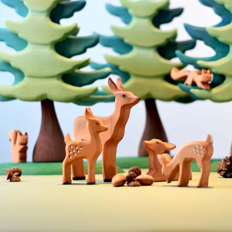 Hand-carved wooden toy animals, including a family of deer with detailed spots, standing among green felt foliage.