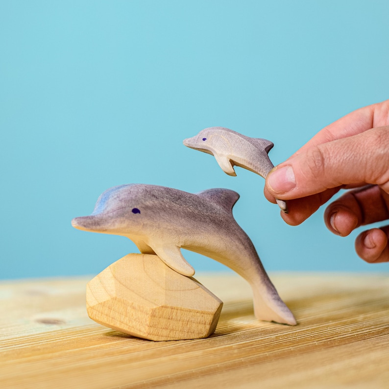 A small wooden dolphin, carefully held by a human hand, represents BumbuToys' commitment to creating tactile, interactive, and environmentally friendly toys that bring the sea’s majesty into your home.