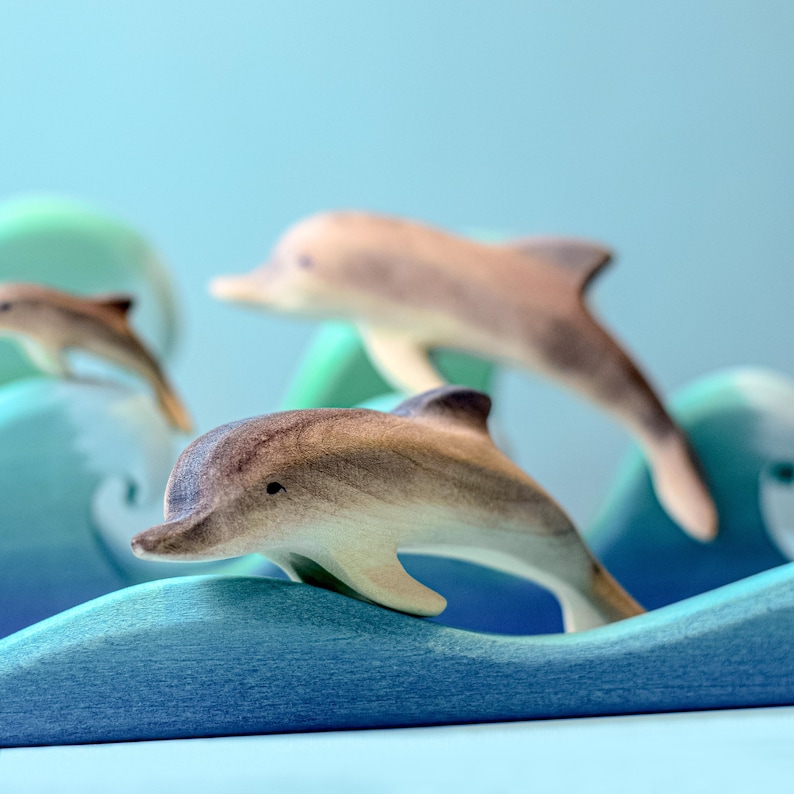 A tableau of wooden dolphins surfing the waves, illustrating BumbuToys' dedication to fostering imaginative play with their handcrafted, eco-conscious wooden toys that capture the essence of marine life.