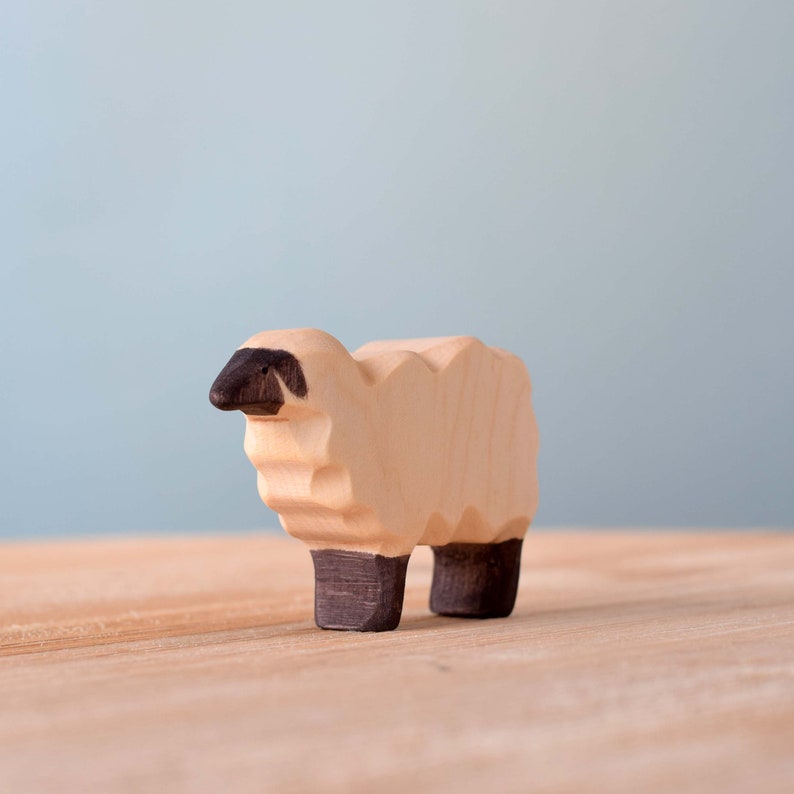 Side view of a wooden sheep toy showcasing its detailed face and dark legs on a wooden surface with a soft blue background.