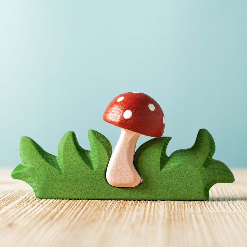 A vibrant red and white spotted wooden mushroom toy emerging from a green wooden grass base.