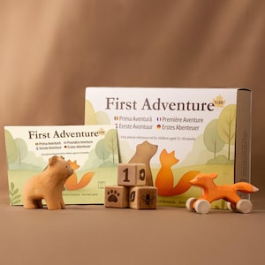 Puede incluir: Un kit de hitos educativos de madera para niños de 12 a 18 meses. El kit incluye una figura de oso, un zorro sobre ruedas, bloques de madera con números y huellas de animales, y cajas con el texto "First Adventure".