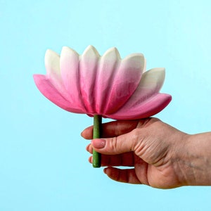 Handmade wooden lotus flower with detailed petal painting in hues of pink and white, set against a serene blue backdrop, held aloft on a leafy base.
