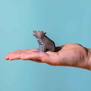 Small wooden figure of a wolf pup seated and tilting its head upwards in a howl, with the craftsmanship highlighted by the natural wood finish and soft blue background.