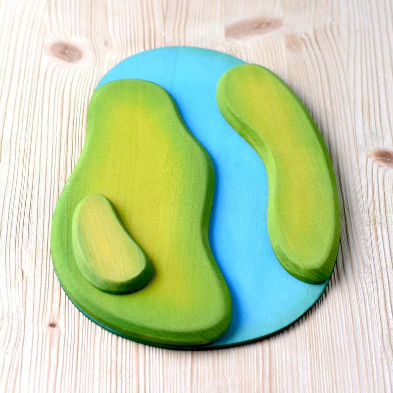Empty green and blue wooden play mat designed to represent a river running through a grassy field on a wood surface.