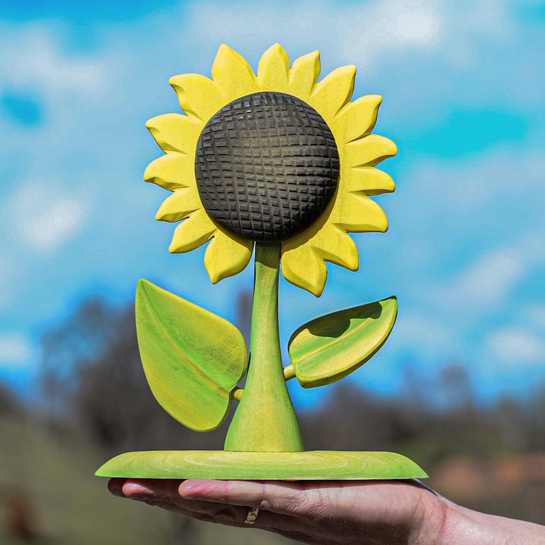 Waldorf inspired sunflower toy cradled in an open palm under blue sky, emphasizing the natural wooden texture