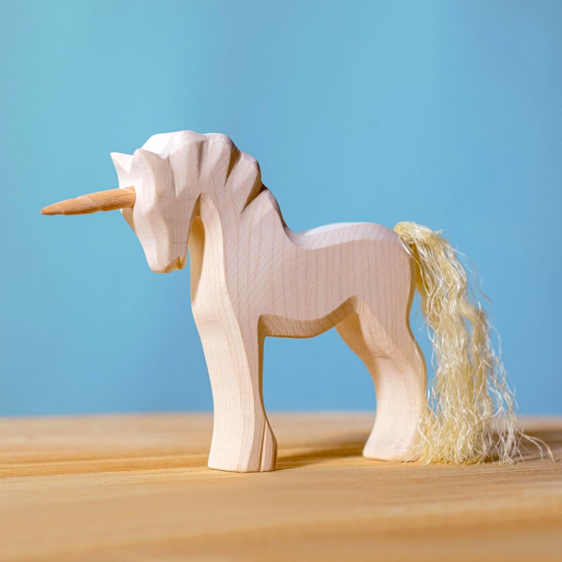 Side view of a wooden unicorn toy with detailed mane and spiral horn on a light wood table with a soft blue backdrop.