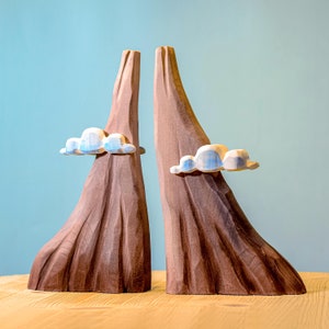 Creative wooden toy set showing a stratovolcano erupting, with striking lava and calming clouds against a pastel blue backdrop.