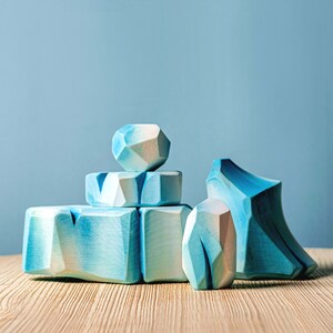 Stacked wooden blocks resembling icebergs with a smooth finish on a wooden surface, and a pale blue wall behind.