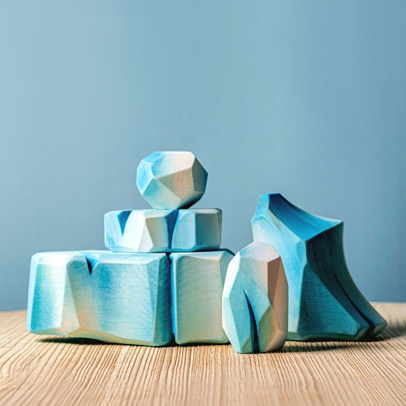 Stacked wooden blocks resembling icebergs with a smooth finish on a wooden surface, and a pale blue wall behind.