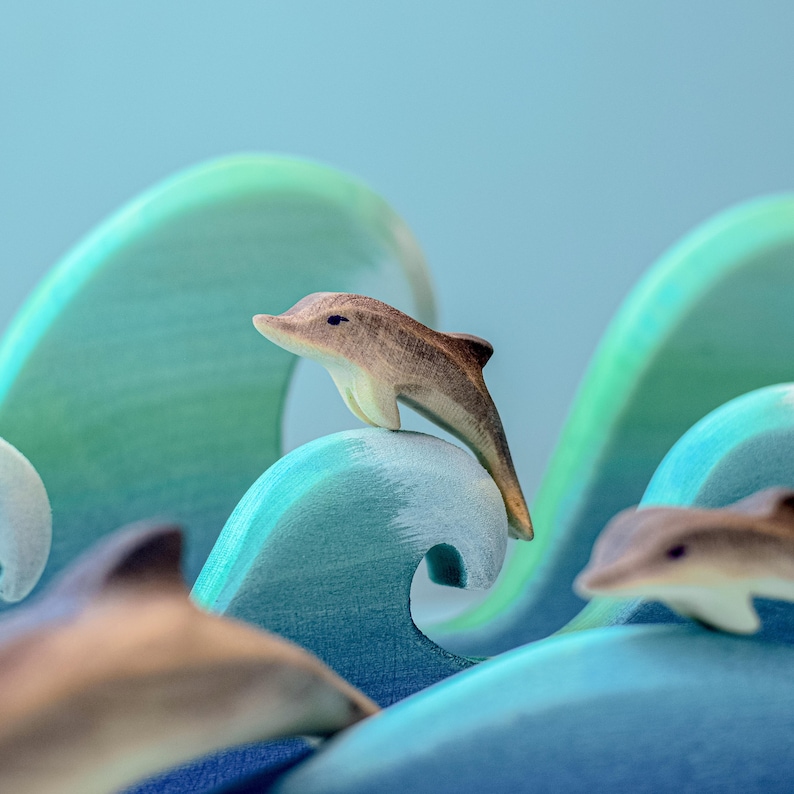 A handcrafted wooden dolphin toy gracefully arches above stylized blue felt waves, capturing the essence of a dolphin in motion with a soft focus background emphasizing its upward movement.