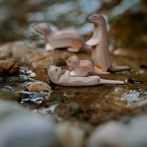 Handcrafted wooden otter family on display, featuring standing and playful poses, with a serene natural background suggesting a waterside habitat.