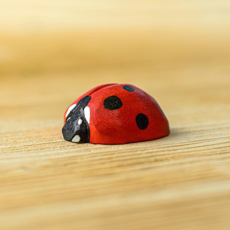 A wooden ladybug toy with red and black detailing resting on a natural wood surface.