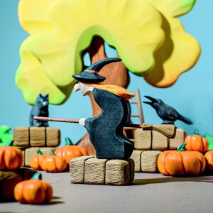 Autumn-themed play scene with a hand-painted cat wooden figure observing a witch character, amidst pumpkins and hay bales.