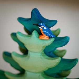 Close-up of a wooden kingfisher toy on a vibrant green tree, exemplifying BumbuToys’ attention to detail in creating realistic and engaging play environments.