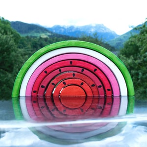 Wooden watermelon stacker toy against a mountainous backdrop, reflecting in water, nature-inspired Montessori toy.