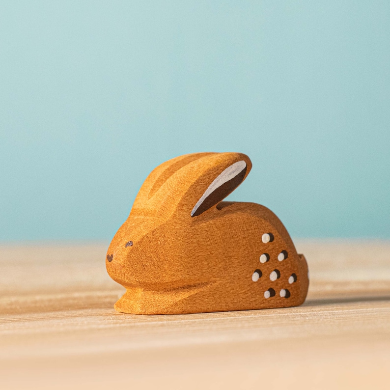 A charming handmade wooden bunny figure with cut-out patterns sits on a smooth surface against a soft blue background.