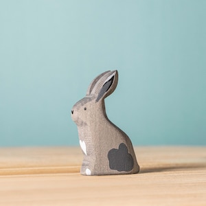 A handmade wooden rabbit figurine with a minimalist design stands on a wooden surface against a soft blue background.