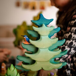 Wooden kingfisher toy perched on a layered green wooden tree, part of a playset by BumbuToys designed for storytelling and learning about bird habitats.