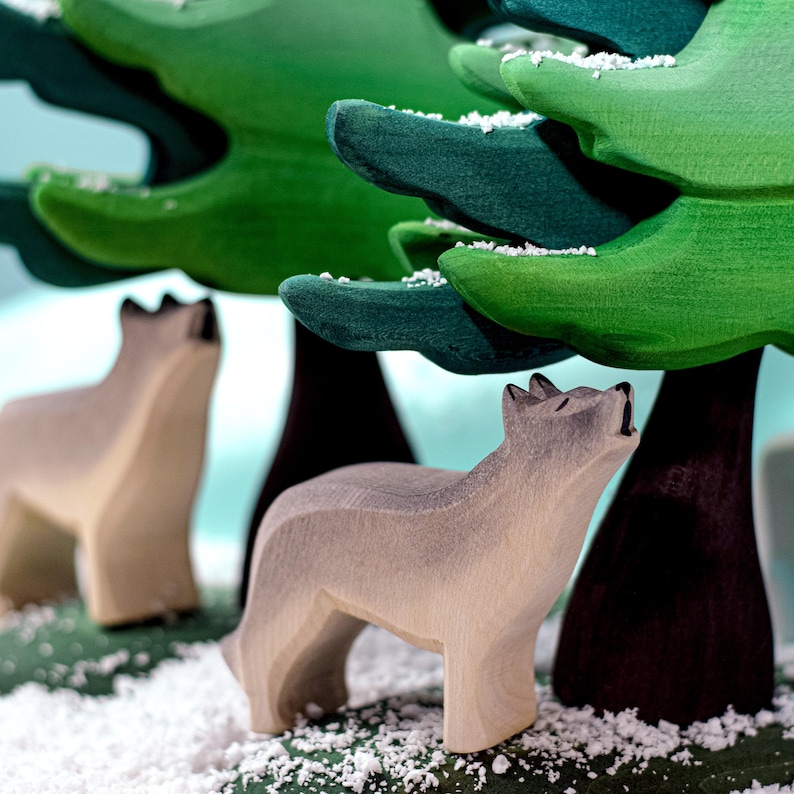 Wooden wolf figurine standing among snowy green trees with other animal figurines.