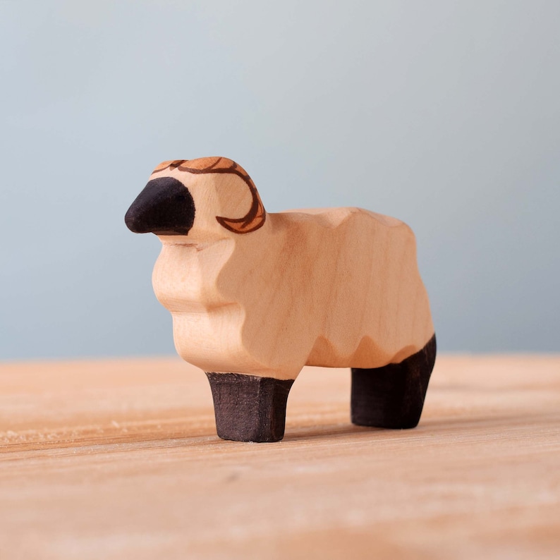 Close-up of a single wooden sheep toy with dark ears and face, and a detailed spiral horn, on a wooden table.