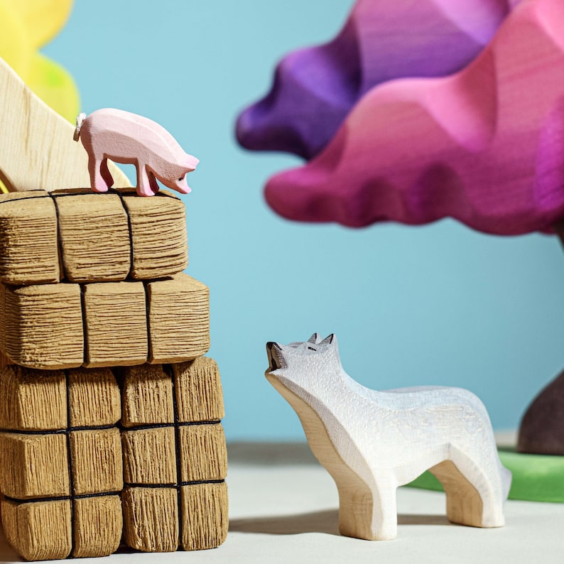 Wooden pig figurine on top of stacked logs with a wolf figurine looking up against a backdrop of colorful trees.