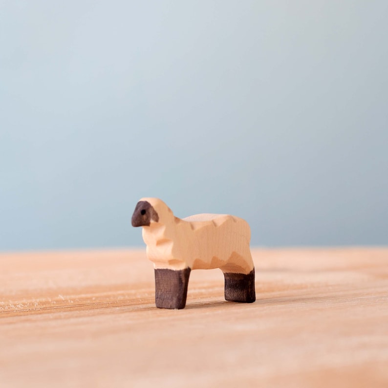 Small wooden sheep figure with black painted legs and face, standing on a wooden surface with a blue background.