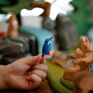 Child's hand gently holding a small wooden kingfisher toy, indicative of BumbuToys’ commitment to creating toys that fit comfortably in the hands of little ones for interactive storytelling.