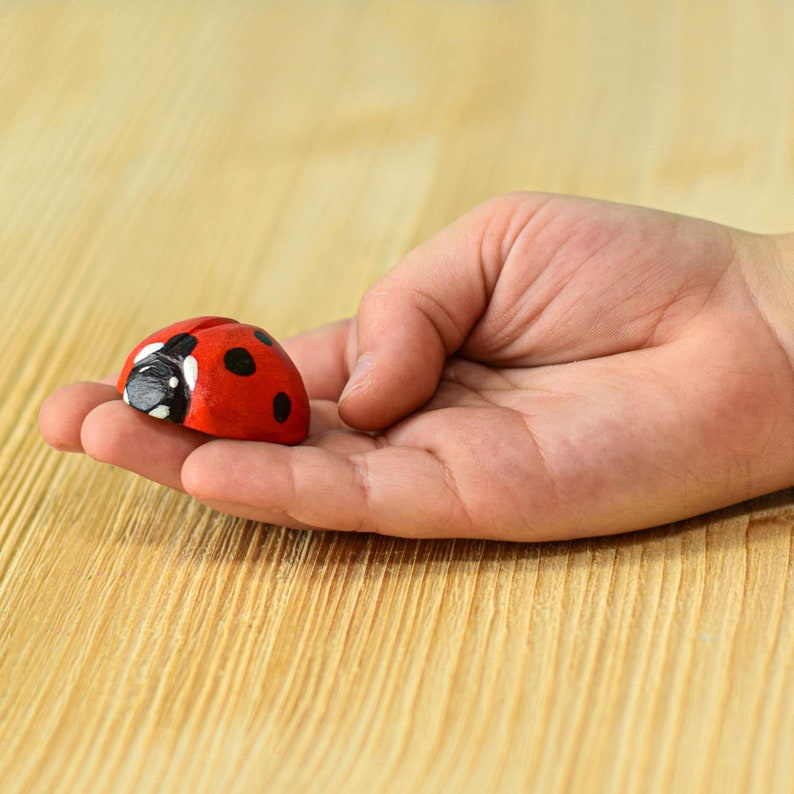 Close-up of a wooden ladybug toy in a child's open palm, showcasing the toy's detailed painting and craftsmanship.