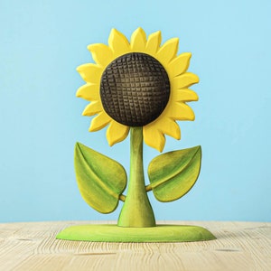 Artisanal Montessori wooden sunflower toy on a green stand displayed on wood with a clear blue background