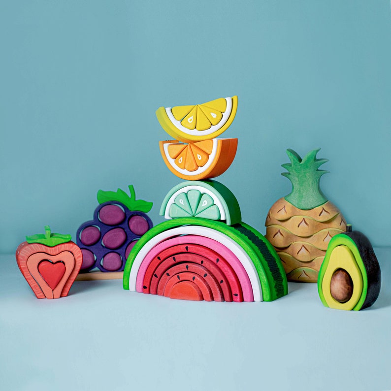 A variety of wooden fruit stacker toys including watermelon, arranged artistically, Montessori-inspired playset.