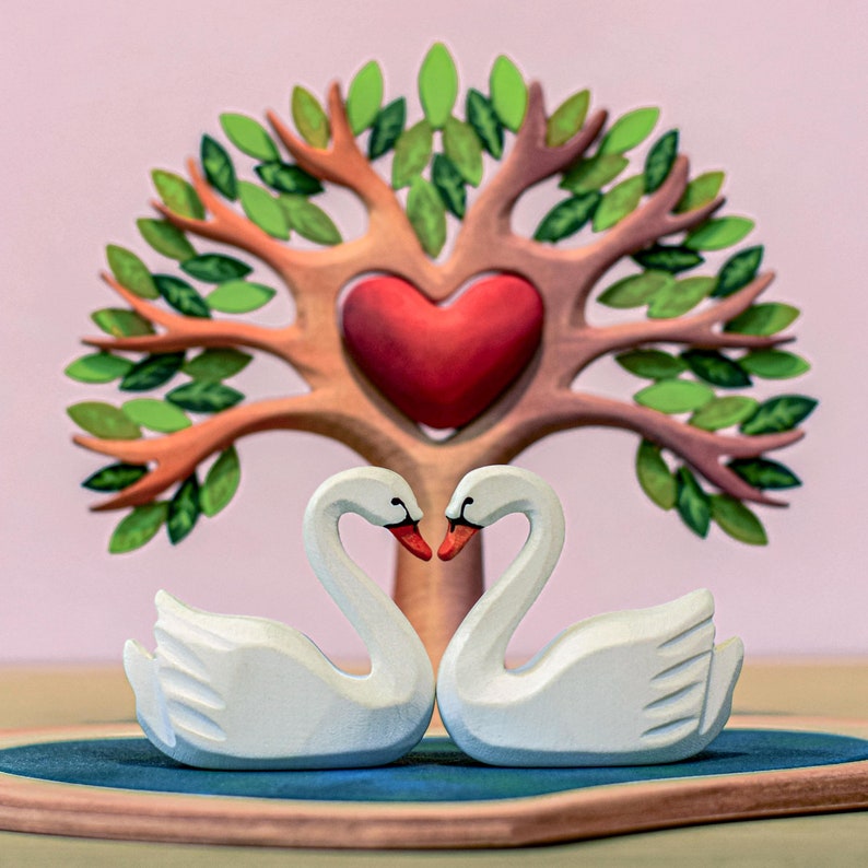 Romantic wooden heart tree toy with two swan figurines forming a heart shape in front, symbolizing love and affection