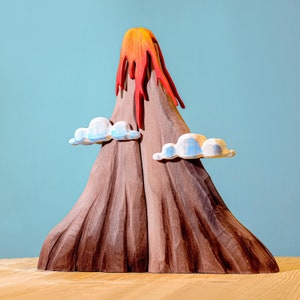 Artisanal playset featuring a wooden volcano in mid-eruption, with colorful lava detail and serene puffy clouds, showcased on a light wood surface.