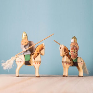 Pair of wooden knights on horses ready for a joust, with one knight carrying a red flag and the other a fox banner, standing side by side on a wooden surface.