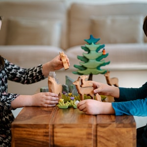 A playful wooden toy scene with deer figures among miniature trees and flowers, suggesting a serene forest environment.