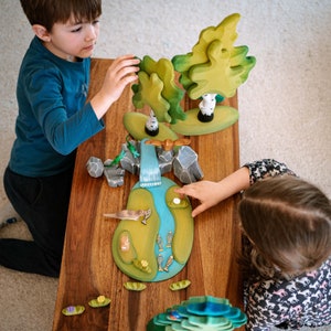 Children engaged in creative play with wooden otter figurines and assorted handcrafted landscape elements, illustrating the toys' interactive and educational value in a home setting.