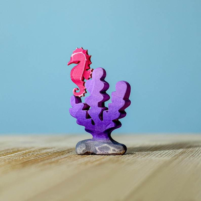 Pink wooden seahorse figurine mounted on a purple coral-shaped stand, adding a pop of color against the blue backdrop.
