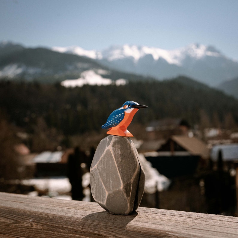 Handcrafted wooden kingfisher toy by BumbuToys, positioned against a scenic mountain backdrop, blending the art of play with the beauty of the natural world.