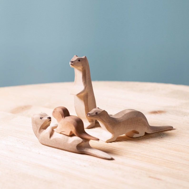 Handcrafted wooden otter family on display, featuring standing and playful poses, with a serene blue background suggesting a waterside habitat.